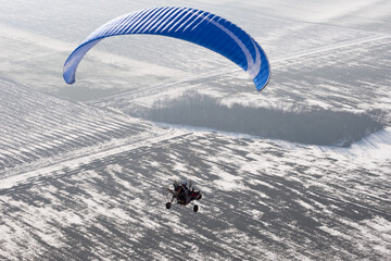 Aerial view paramotor buggy or motorized paraglider seen from the sky in France and flying over snowy fields in winter