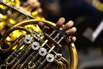 Hands of a musician playing the French horn in the orchestra close up