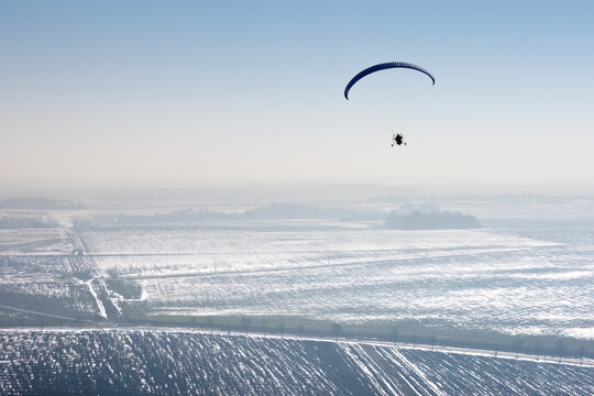 paramotor seen from the sky in France flying over snowy fields in winter with horizon and blue sky