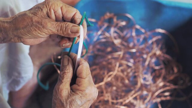 Closeup of elderly wrinkling hands remove copper from old wires plastic cover. Pre-process of recycling metal garbage. Environmental awareness. 