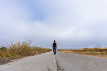 Faceless person walking in a road surrounded by the countryside.