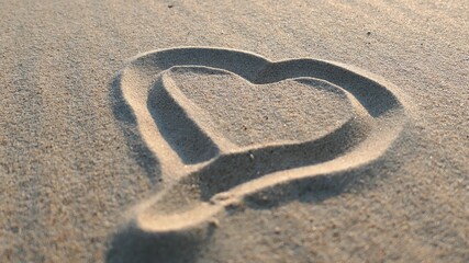 Fototapeta na wymiar Heart Shapes Being Drawn on Sandy Beach and Wiped Out by Sea Wave at Sunset