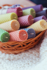 Fototapeta na wymiar Set of colored decorative natural beewax candles with a honey aroma for interior in a brown basket near lavender on a white knitted sweater. Close up. A delicate color palette. Selective focus
