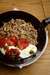 Boiled buckwheat with mushrooms and tomatoes on a wooden background. Dish in a frying pan close-up.