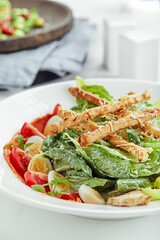 Caesar salad with bread sticks, quail eggs, cherry tomatoes and grilled chicken in plate on white background