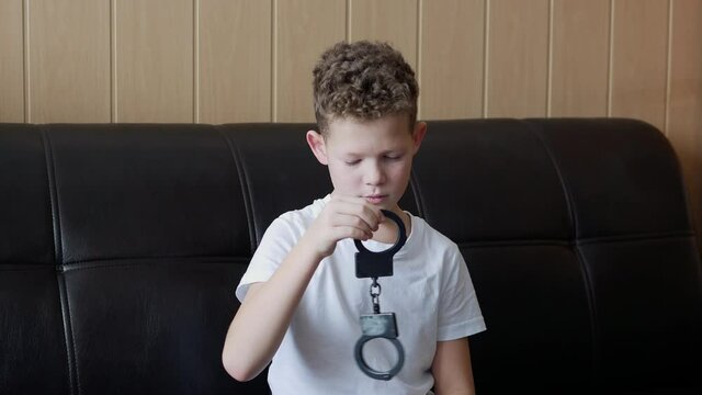 curly boy holding handcuffs in his hand looks at them
