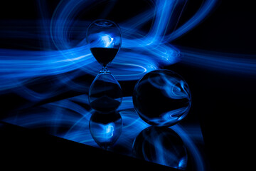 Glass crystal ball and sand clock on a mirror, with a electric blue light painting fractals