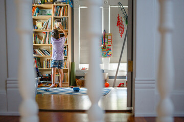 View through stair railing of a boy exploring a tall bedroom bookshelf
