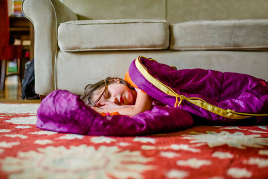 A beautiful little girl rests in a sleeping bag on the floor indoors