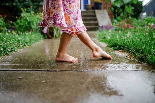 close-up of a small barefoot child dancing on front stoop in the rain