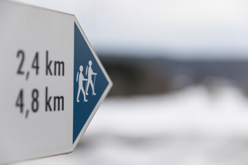 Wanderschild mit Kilometerangaben in Winterlandschaft mit Schnee.