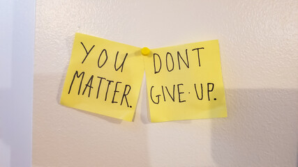 You matter, don't give up encouragement phrase written on two yellow sticky notes posted on a white...