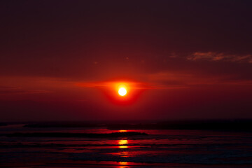 Winter dark red burning sunset over frozen river with red reflection on ice surface