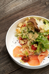 Caesar salad with salmon fish on white bowl