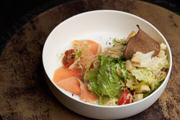 Caesar salad with salmon fish on white bowl