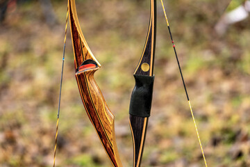 Close-up of two archery bows made of wood called longbow on a blurred landscape. Archery sport...