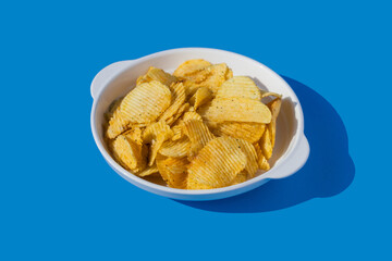 Potato chips fall into a white plate on a blue background. Flying chips.