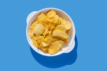 Potato chips fall into a white plate on a blue background. Flying chips.