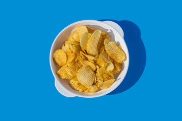 Potato chips fall into a white plate on a blue background. Flying chips.