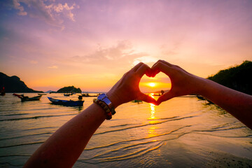 Female hands in the form of heart  in sunset sky at the sea