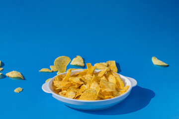 Potato chips fall into a white plate on a blue background. Flying chips.