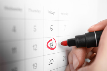 Woman marking Friday 13th on calendar, closeup. Bad luck superstition
