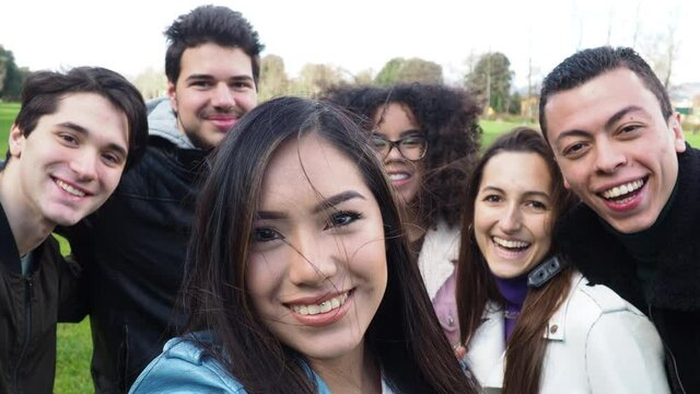 Group of friends making a selfie with smartphone at the park - Millennials having fun together in the field - Multiethnic people post a video footage on social network