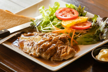close up roasted chicken steak with gravy sauce, there are bread and salad with cream sauce on side dishes