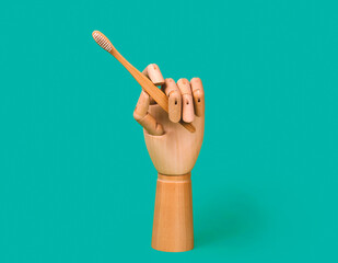 Wooden mannequin hand holding bamboo toothbrush. Dental care concept. Isolated on blue background.