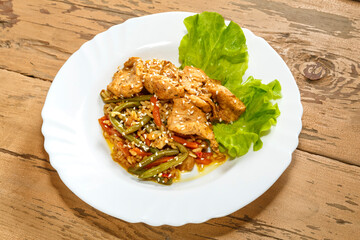 Vegetables with rice and chicken in sauce and sesame seeds on salad leaves on a wooden table in a plate.