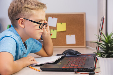 Schoolboy with glasses studies at home with laptop. Home learning, online education.