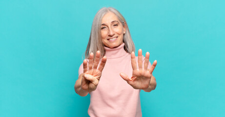 middle age woman smiling and looking friendly, showing number nine or ninth with hand forward,...