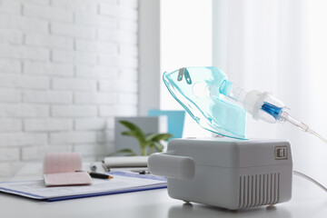 Modern nebulizer with face mask on white table indoors, space for text. Inhalation equipment
