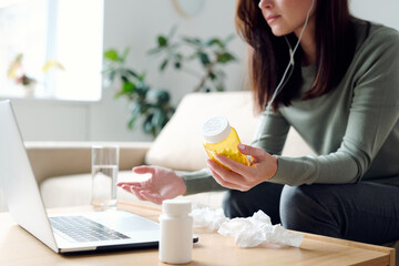 Sick female holding bottle of pills while consulting with online doctor