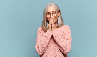 middle age woman happy and excited, surprised and amazed covering mouth with hands, giggling with a...