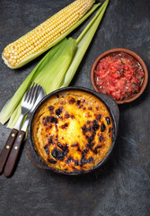 Chilean food. Traditional Pastel de Choclo corn pie. Beef meat with onion, chicken and egg covered with ground corn in clay bowl, top view