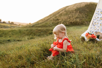 cute little girl is having fun near wigwam in a summer field on sunset. Young family spending time together on vacation, outdoors. The concept of summer holiday. © Andriy Medvediuk