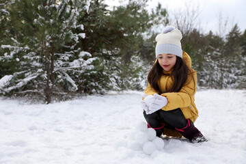 Fototapeta na wymiar Cute little girl rolling snowballs in winter forest