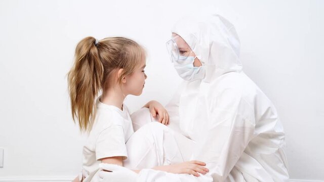 A little girl hugs a doctor in a white protective suit, mask, glasses and gloves