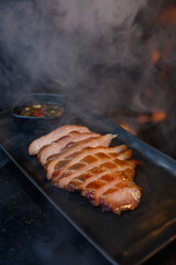 Smoked Pork or meat Steak with chili sauce put on black plate.