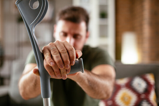Young man with a hand on his crutches sitting on sofa. Man having back pain..