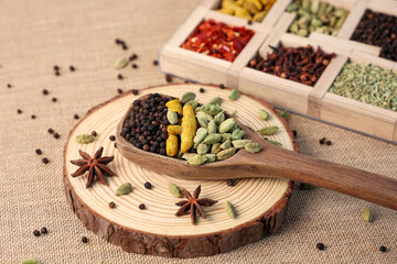 Indian spices for Indian cooking Masala for hot and spicy curry , whole spices turmeric, cardamom, black pepper in wooden spoon, star anise , paprika in Indian spice box  Kerala India Sri Lanka.
