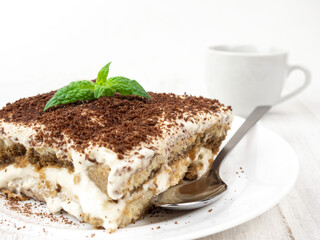 Tiramisu cake with mint leaf on a plate on a light background.