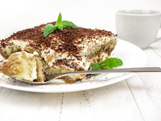 Tiramisu cake with mint leaf on a plate on a light background.