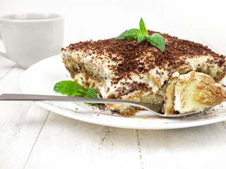 Tiramisu cake with mint leaf on a plate on a light background.