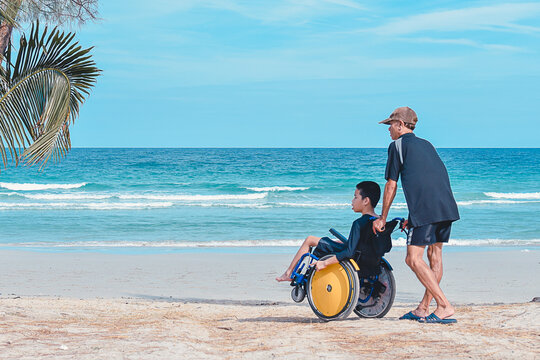 Father and Special child on wheelchair playing,doing activity vacation on  sea beach in summer, Lifestyle of disability child, Life in the education age, Happy disabled kid in travel holidays concept.