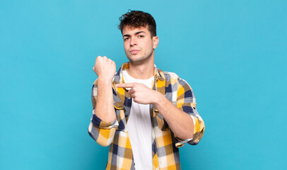young man looking impatient and angry, pointing at watch, asking for punctuality, wants to be on...