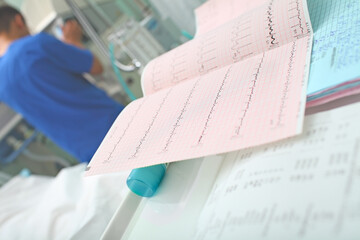 ECG tracing and other test results at the nursing station on the background of working male doctor in the ICU