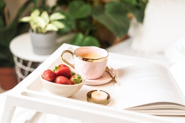  Breakfast in bed. Heart shaped white plate with fresh strawberries, cup of coffee, book and plants flowers. Still life composition. Mother, Valentine day concept.