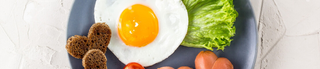 banner of Fried eggs in the shape of a heart with sausages, herbs and tomatoes. Breakfast on Valentine's day